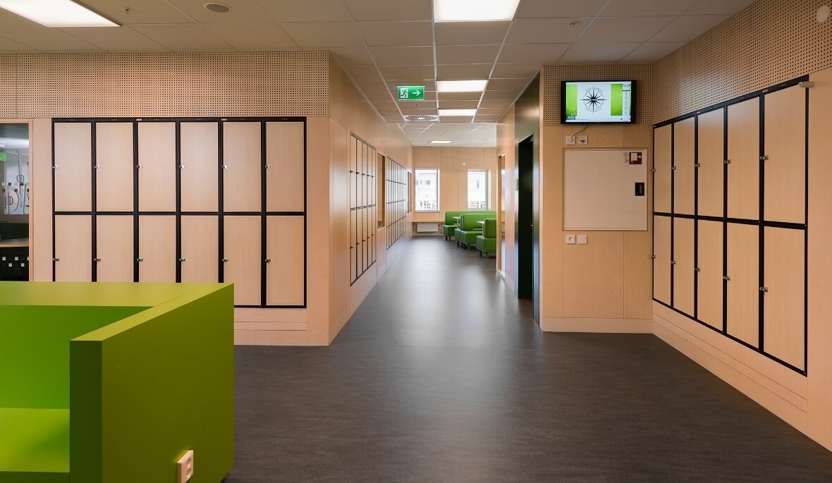 Et lærerværelse med grøn sofa, sort laminatgulv og garderobeskabe indenfor alle vægge rundt i lokalet og gangene rundt.